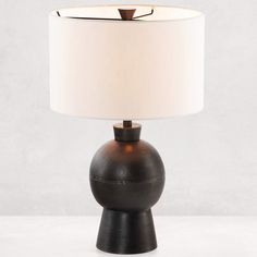 a black table lamp with a white shade on the base and a light bulb in the middle