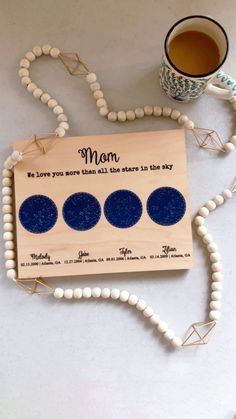 a wooden plaque with three blue circles on it next to a coffee cup and bead necklace