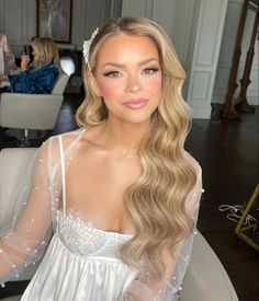 a woman with long blonde hair sitting in a chair wearing a white dress and pearls on her head