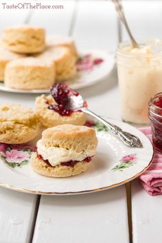 scones with jam and cream on them are sitting on plates next to a jar of jelly