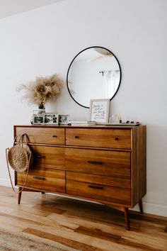 a wooden dresser with a mirror on top of it and a wicker basket in front of it