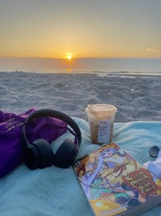 a book and headphones on a blanket at the beach with a cup of coffee