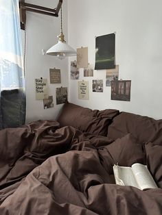 an unmade bed with brown sheets and pictures on the wall above it, along with a lamp