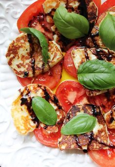 grilled tomatoes and mozzarella with basil leaves on a white plate, ready to be eaten