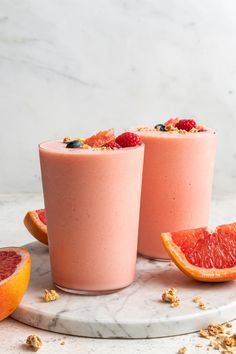 two glasses filled with pink smoothie next to sliced grapefruit