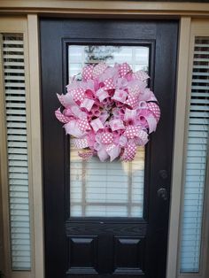 a pink and white polka dot wreath on a black door with shutters in the background