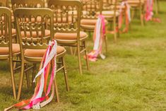 rows of chairs with ribbons on them in the grass at an outdoor wedding ceremony,