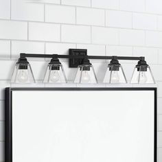 a bathroom mirror with three lights on it and a white brick wall in the background