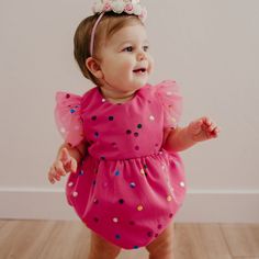 a baby girl wearing a pink dress with polka dots on it's chest and a bow in her hair