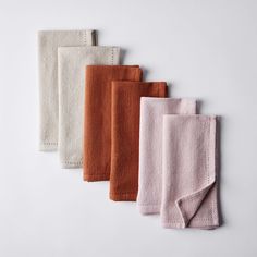 five different colored towels are lined up on a white surface with one folded in half