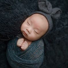 a newborn baby wearing a knitted hat and sleeping on a black furnishing