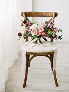 a wooden chair with flowers on it and a white table cloth draped over the seat