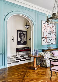 a living room filled with furniture and a chandelier hanging from the ceiling in front of a painting