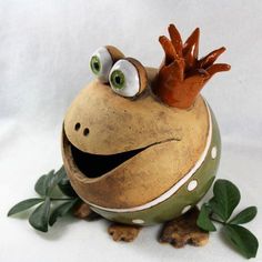 a ceramic frog with googly eyes sitting on top of leaves