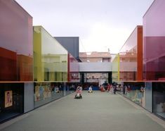 people are walking through an open area with colorful glass walls on either side and in the middle