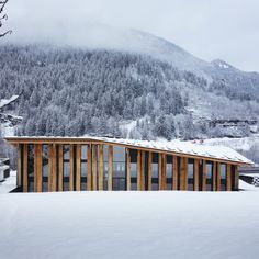 a house in the middle of a snow covered field with mountains in the back ground