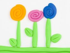 three colorful flowers sitting next to each other on top of a white surface with green stems