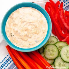 a bowl of dip surrounded by sliced cucumbers, carrots and red peppers