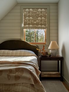 a bed sitting under a window next to a night stand with a lamp on it