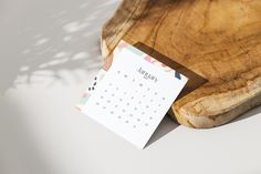 a calendar sitting on top of a wooden cutting board next to a piece of wood