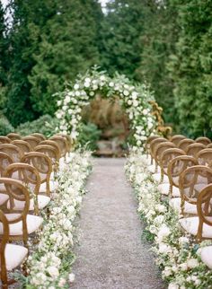 rows of chairs with white flowers and greenery lining the aisle at an outdoor wedding ceremony