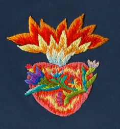 an embroidered heart with flowers and leaves in the shape of a flower on a blue background