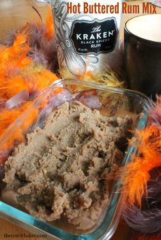 hot buttered rum mix in a glass dish with feathers around it and a bottle of rum