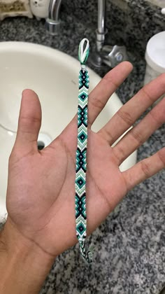 a person's hand holding a bracelet in front of a sink