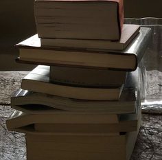 a stack of books sitting on top of each other in front of a glass vase