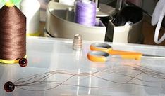 some scissors and thread on a table with other crafting supplies in the back ground