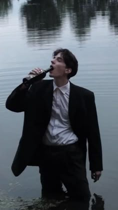 a man in a suit and tie drinking from a bottle while standing in the water