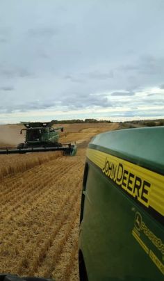 a large green truck driving down a dirt road next to a field filled with crops