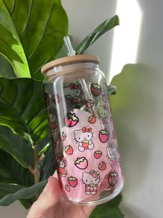 a hand holding a glass cup with hello kitty on it