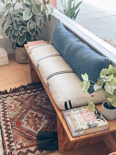 a wooden bench sitting on top of a rug next to a window sill filled with potted plants