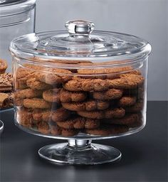 a glass container filled with cookies on top of a table next to two containers full of cookies