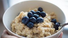 a bowl filled with oatmeal and blueberries in someone's hand