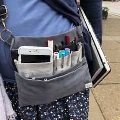 a person holding a cell phone in their pocket with some pens and pencils on it