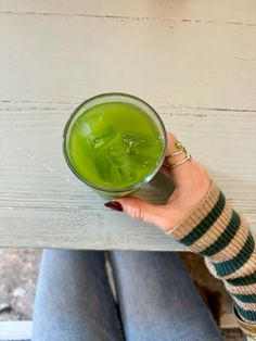 a woman's hand holding a glass of green liquid