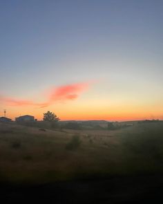 the sun is setting over a field with houses in the distance and trees on the other side