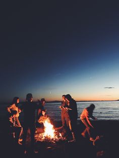 several people standing around a campfire on the beach