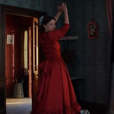 a woman in a long red dress is standing by a door and reaching up into the air