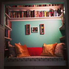 a room with bookshelves filled with lots of books and pillows on top of it