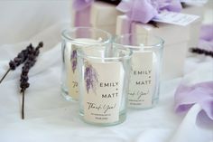 three candles are sitting next to each other on a white tablecloth with purple flowers