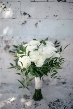 a bouquet of white roses sitting on top of a table next to a brick wall