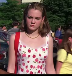 a girl in a floral dress is standing near other people and looking at the camera