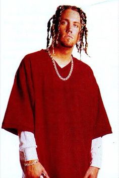 a man with dreadlocks standing in front of a white wall wearing a red shirt