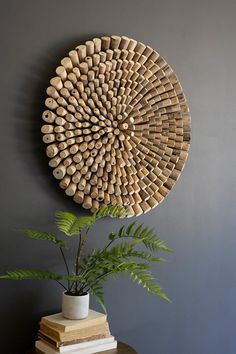 a round wooden wall hanging on the side of a gray wall next to a potted plant