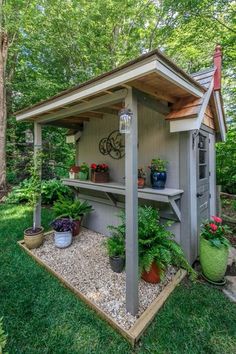 a small shed with potted plants on the outside and in the inside, is surrounded by trees