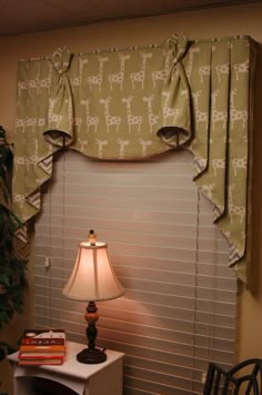 a lamp sitting on top of a table next to a window covered in roman shades