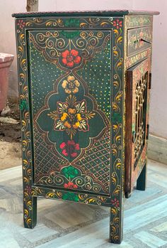 an ornately painted cabinet sits on the floor in front of a potted plant